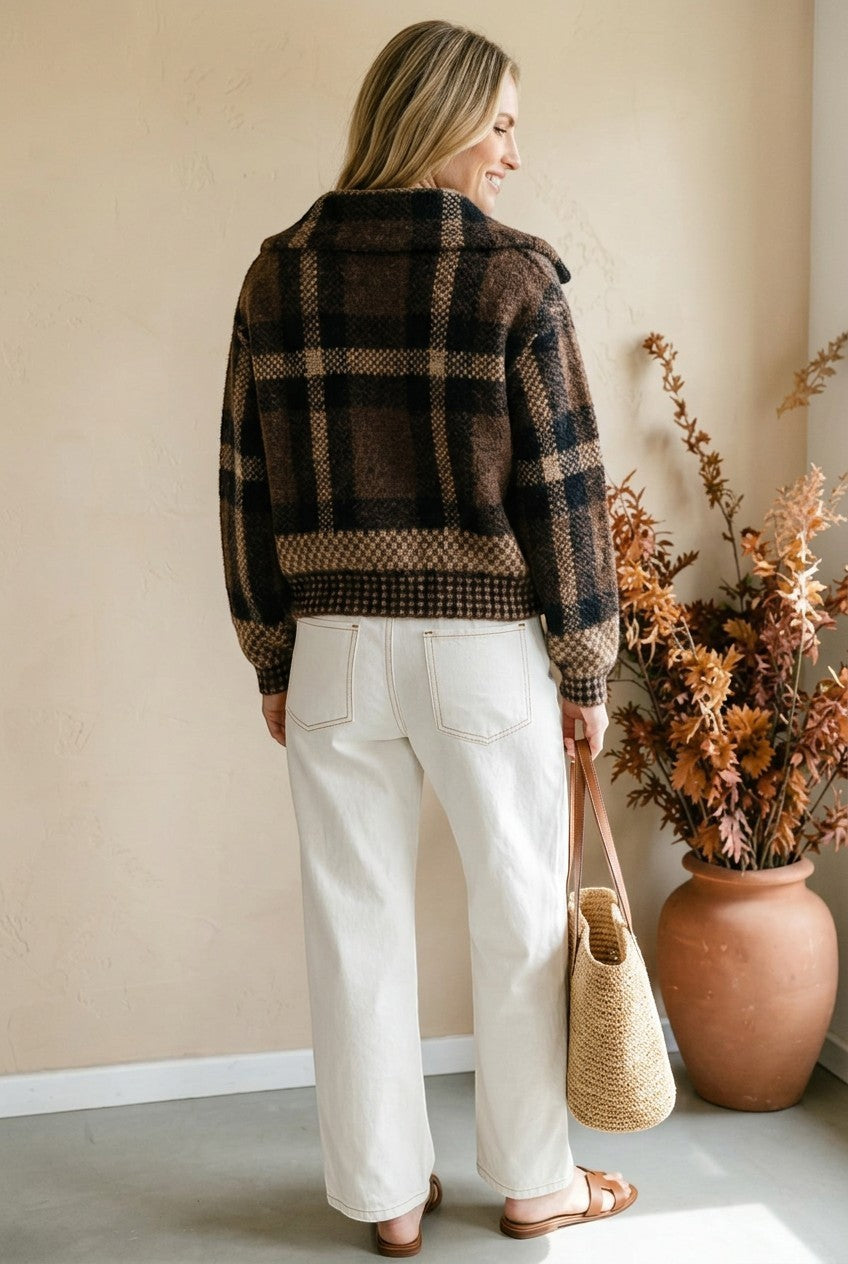 Model wearing a graced brown and black plaid button-down cardigan with white jeans and a straw tote bag