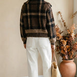 Model wearing a graced brown and black plaid button-down cardigan with white jeans and a straw tote bag