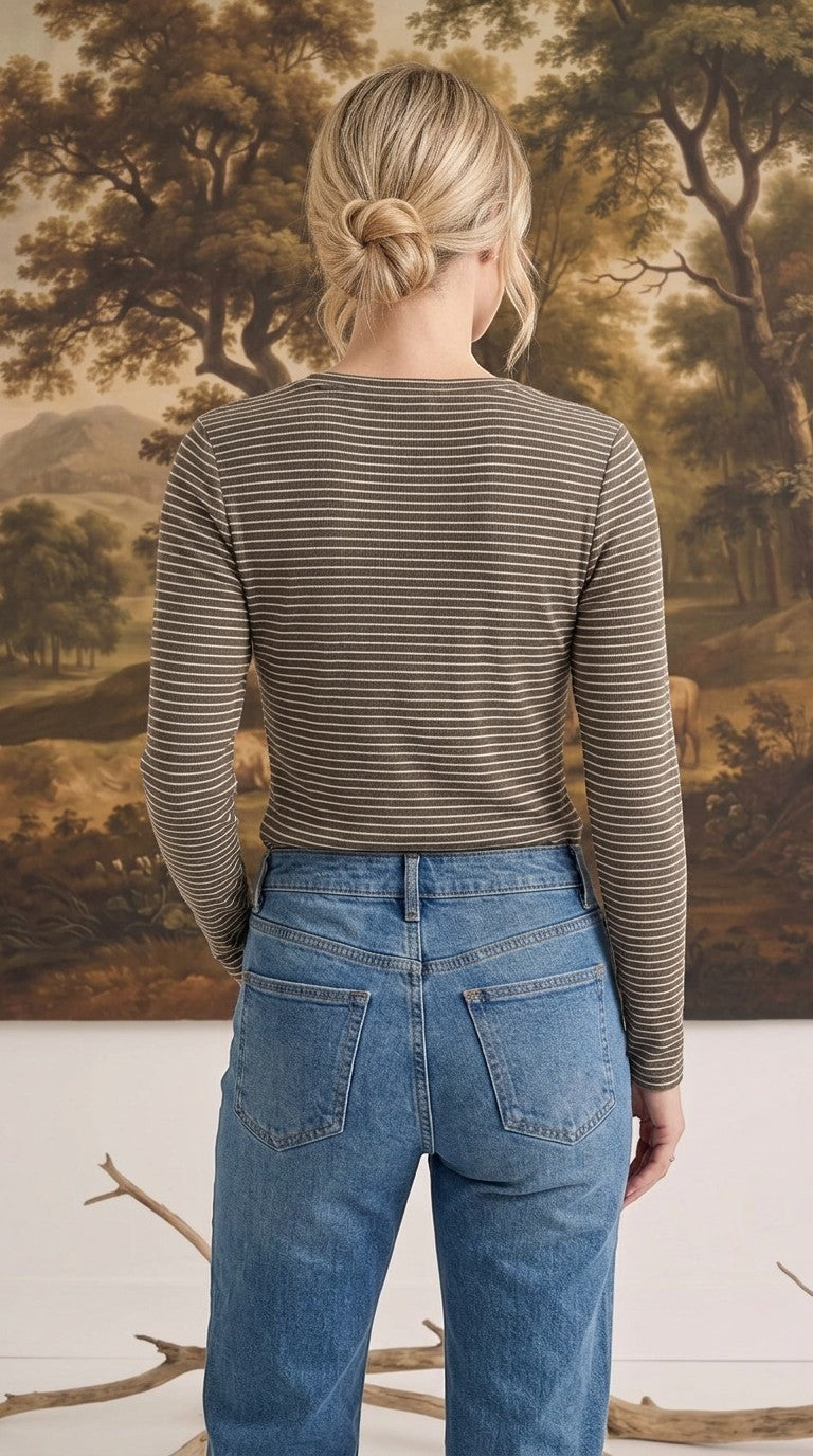Back view of a woman wearing a graced brown and white horizontal striped long sleeve top with blue denim jeans