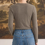 Back view of a woman wearing a graced brown and white horizontal striped long sleeve top with blue denim jeans