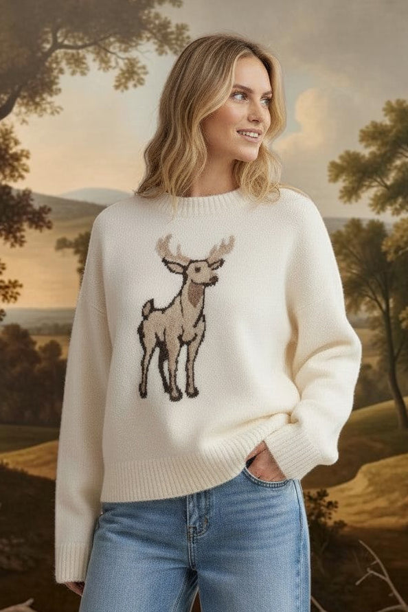 A woman wearing a cream graced deer graphic sweater with blue jeans in a sunlit room.