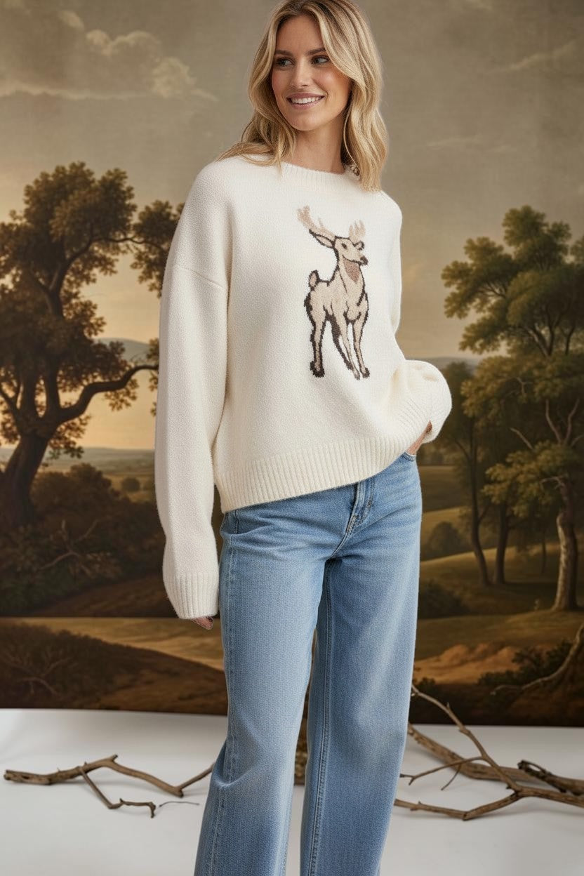 Model wearing a cream graced deer graphic sweater with a soft knit texture, paired with light wash blue jeans.