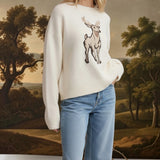 Model wearing a cream graced deer graphic sweater with a soft knit texture, paired with light wash blue jeans.