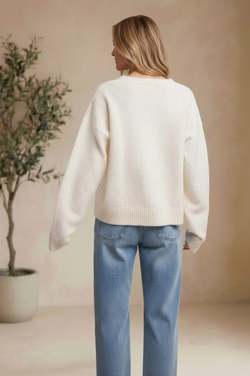 Back view of a woman wearing a cream-colored graced knit sweater with long sleeves and ribbed hem paired with blue jeans.