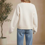 Back view of a woman wearing a cream-colored graced knit sweater with long sleeves and ribbed hem paired with blue jeans.