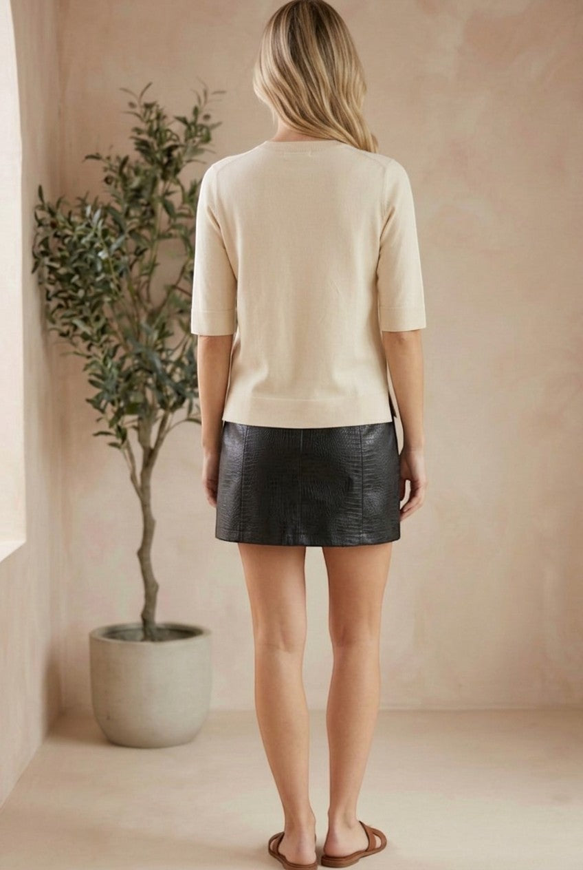 Back view of a model wearing a graced cream short sleeve knit top paired with a black mini skirt