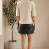 Back view of a model wearing a graced cream short sleeve knit top paired with a black mini skirt