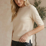 Model wearing a graced cream short sleeve knit top with a crew neckline and side slits, paired with a black skirt.