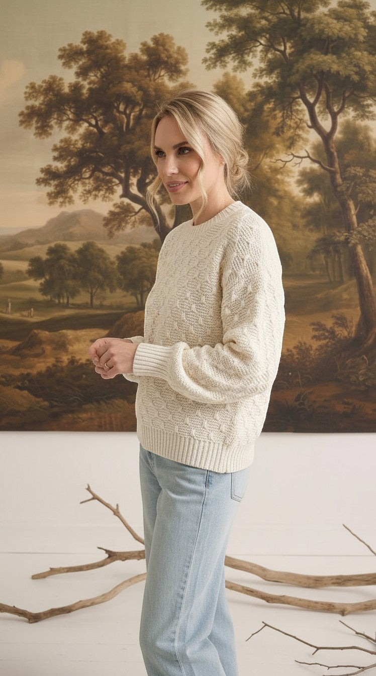 A woman wearing a cream-colored graced two-tone textured weave sweater with a relaxed fit and ribbed cuffs.