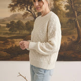 A woman wearing a cream-colored graced two-tone textured weave sweater with a relaxed fit and ribbed cuffs.