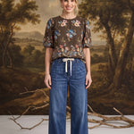 graced dark denim wide-leg pants with a tie-front waist worn by a model with a floral brown blouse