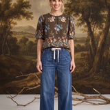 graced dark denim wide-leg pants with a tie-front waist worn by a model with a floral brown blouse
