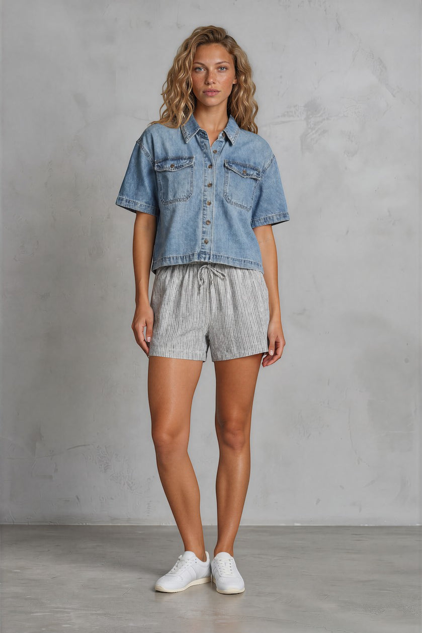 graced light wash denim shirt with short sleeves, two chest pockets, and button front, worn by a woman.