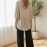 graced dolman long sleeve knit sweater in pebble beige worn by a woman with black wide-leg trousers