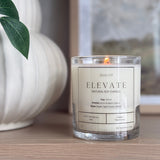 Graced Elevate natural soy wax candle in a clear glass jar with a lit wick, ideal for home fragrance and ambiance.