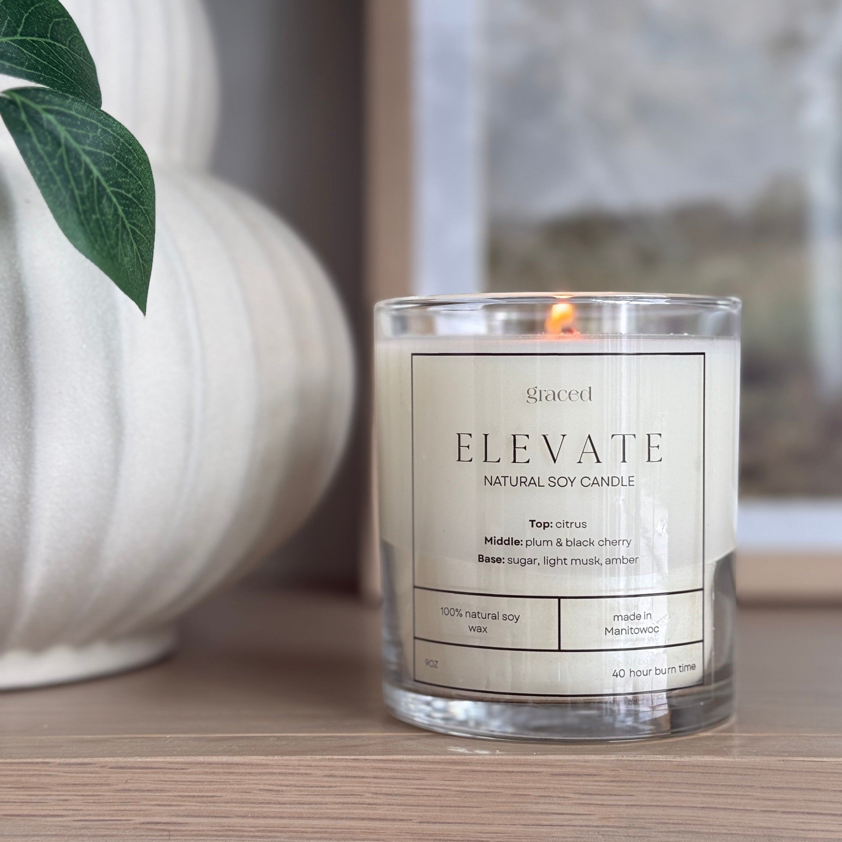 Graced Elevate natural soy wax candle in a clear glass jar with a lit wick, ideal for home fragrance and ambiance.