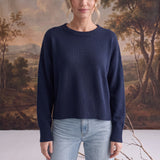 A model wearing a navy graced Eloise crew neck sweater with dropped shoulders and ribbed hem paired with blue jeans.