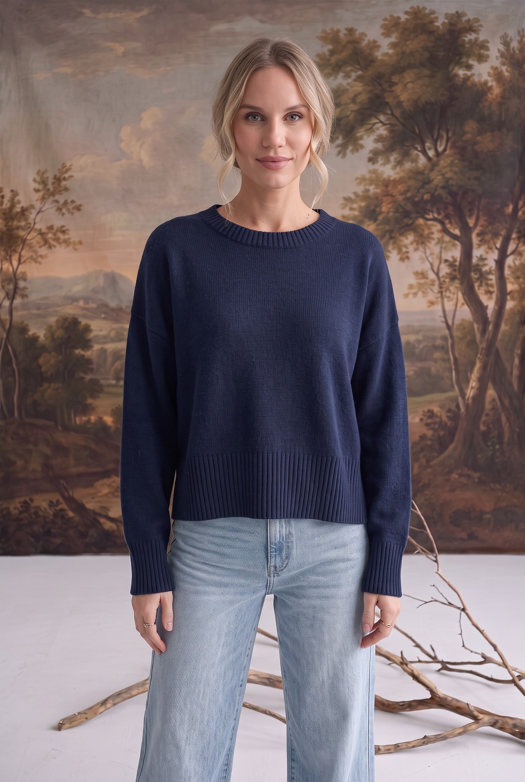 A model wearing a navy graced Eloise crew neck sweater with dropped shoulders and ribbed hem paired with blue jeans.