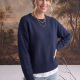 A woman wearing a navy graced Eloise crew neck sweater with dropped shoulders and ribbed hem over a white shirt.