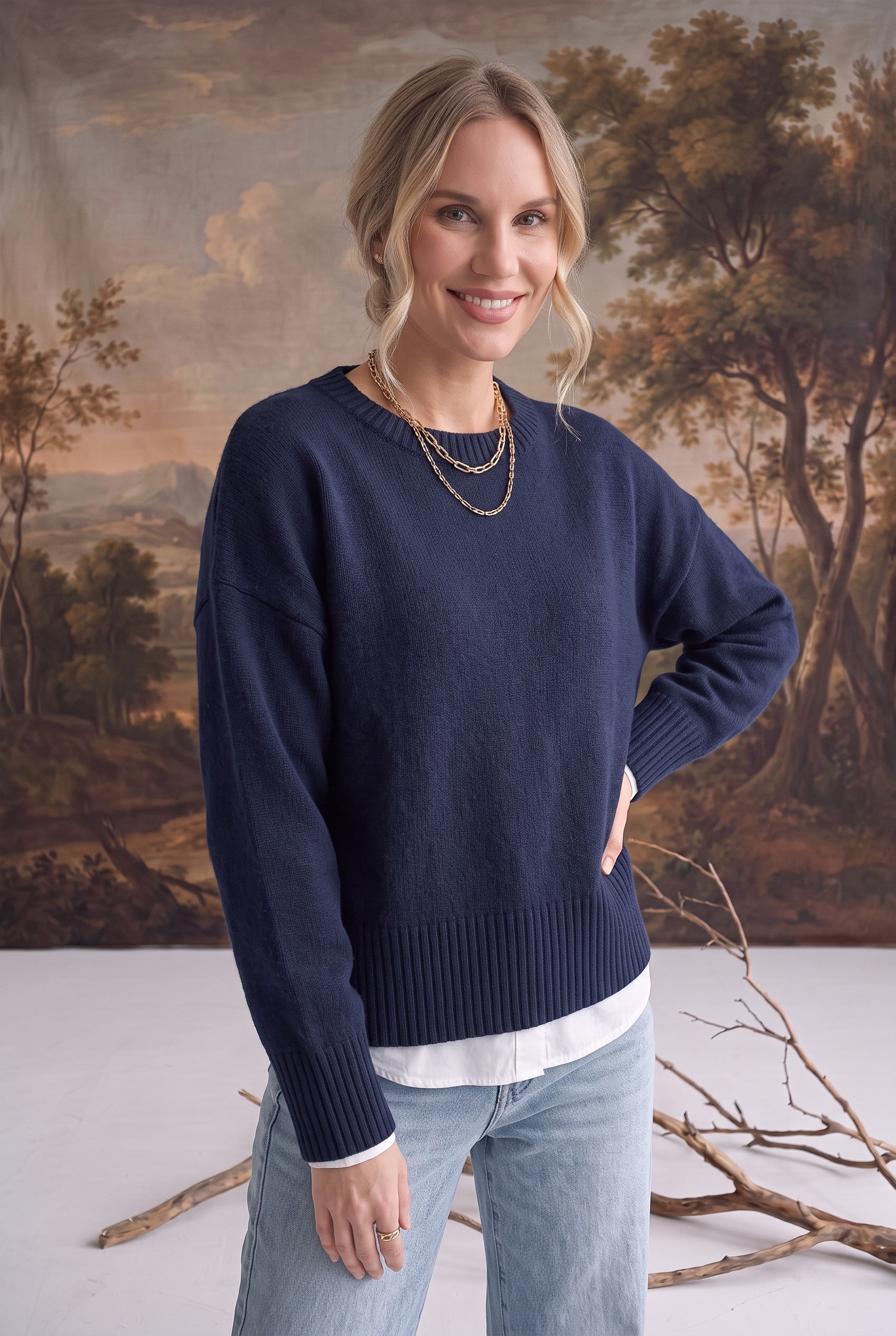 A woman wearing a navy graced Eloise crew neck sweater with dropped shoulders and ribbed hem over a white shirt.