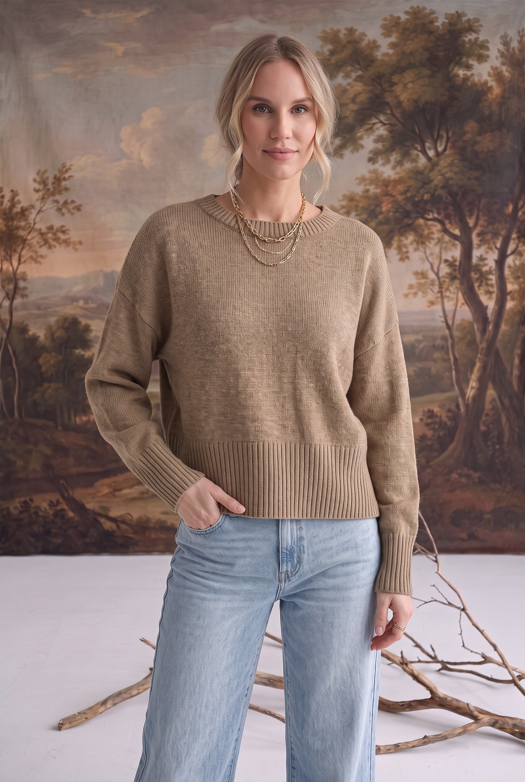 Model wearing a taupe graced Eloise crew neck sweater with dropped shoulders and wide ribbed hem, paired with denim.