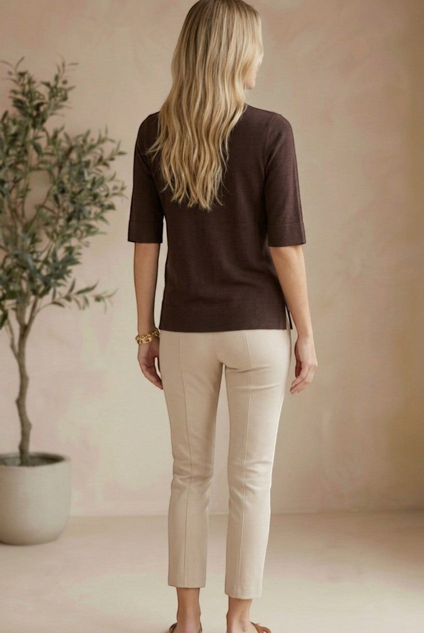 Woman wearing a graced espresso brown short sleeve knit top with beige trousers, viewed from the back.