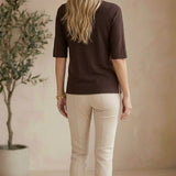Woman wearing a graced espresso brown short sleeve knit top with beige trousers, viewed from the back.
