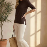 Model wearing a graced espresso brown short sleeve knit top with side slits, paired with beige trousers and sandals.