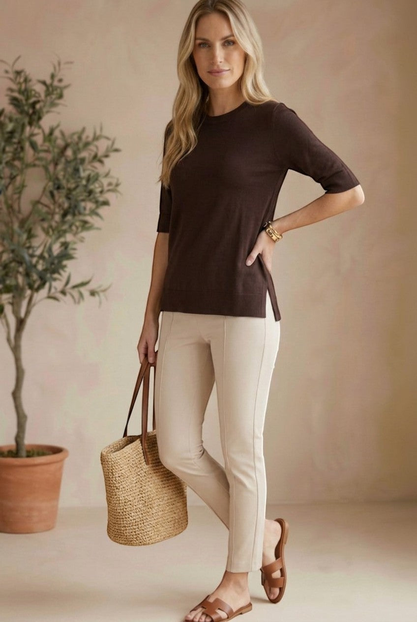 A model wearing a graced espresso brown short sleeve knit top with side slits, paired with beige trousers.