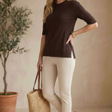 A model wearing a graced espresso brown short sleeve knit top with side slits, paired with beige trousers.