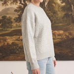 A woman wearing a graced light grey pullover sweater with delicate white floral embroidery on the sleeve and front.