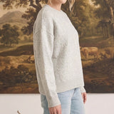 A woman wearing a graced light grey pullover sweater with delicate white floral embroidery on the sleeve and front.