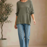 graced forest green dolman long sleeve knit sweater with a chest pocket worn by a smiling woman with blue jeans