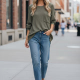 graced forest green dolman long sleeve knit sweater with a chest pocket worn by a smiling woman with blue jeans