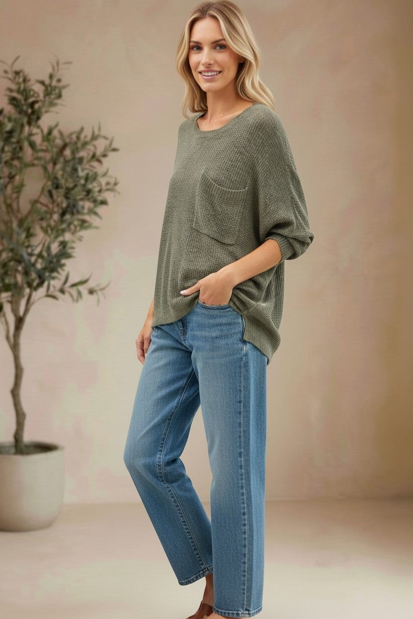 Model wearing a graced forest green dolman long sleeve knit sweater with a chest pocket and relaxed fit with blue jeans