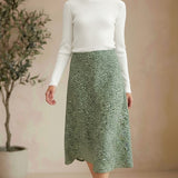 Model wearing a graced green floral print midi skirt with a white ribbed top and brown sandals in a studio setting.