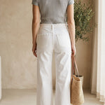 graced High Rise Wide Leg Jeans in white cotton blend with frayed hem. Model wears them with a grey ribbed top and brown sandals.