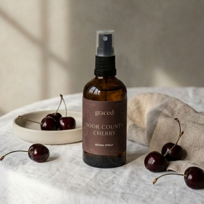 Brown spray bottle labeled 'graced' on a white surface with cherries