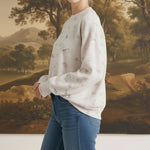 A woman wearing a graced cream-colored long-sleeve top with a subtle horse motif and quilted texture.
