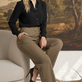 A woman wearing graced houndstooth knit straight pants and a black blouse, sitting on a chair in a studio setting.