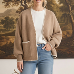 Model wearing a graced The Judy Open Cardigan in beige with white contrast stitching and front pockets over jeans.