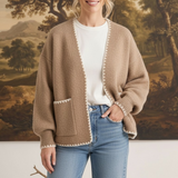 Model wearing a graced The Judy Open Cardigan in beige with white contrast stitching and front pockets over jeans.