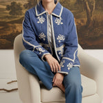 graced The Lea blue cotton jacket with white contrast floral embroidery, worn by a model sitting in a chair.