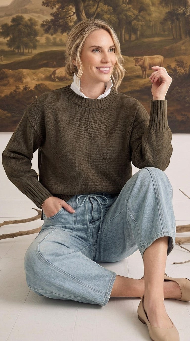 A model wearing graced soft denim barrel pants in light blue with a drawstring waist and a dark olive knit sweater.