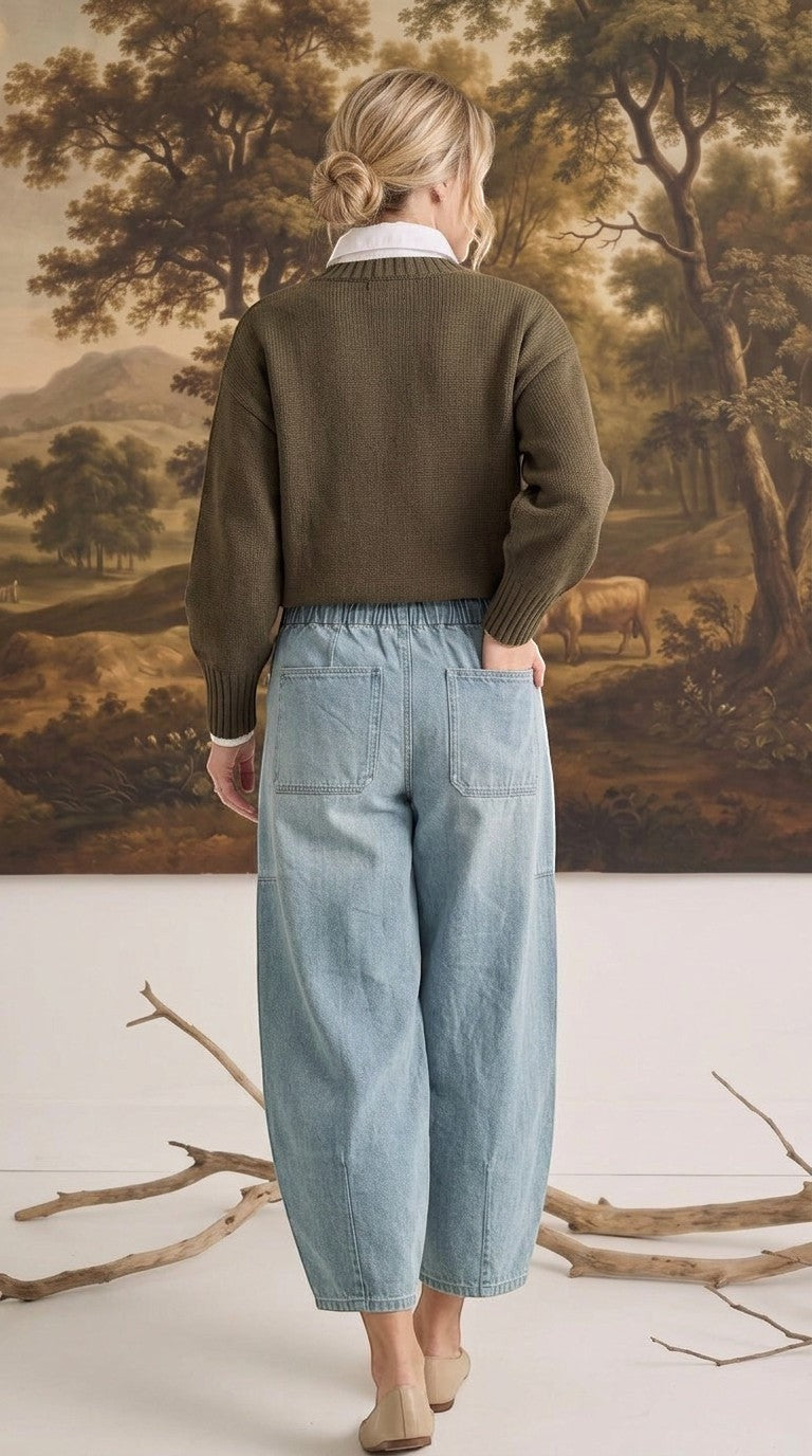 A woman wearing graced light wash denim barrel pants with a relaxed fit and back pockets, styled with an olive sweater.