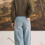 A woman wearing graced light wash denim barrel pants with a relaxed fit and back pockets, styled with an olive sweater.