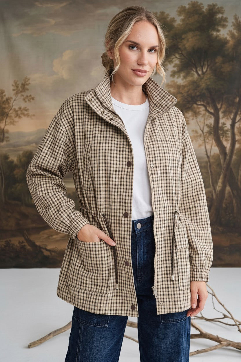 Model wearing a graced Macy mock neck jacket in a beige and brown gingham check pattern with a drawstring waist.