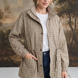 Model wearing a graced Macy mock neck jacket in a beige and brown gingham check pattern with a drawstring waist.