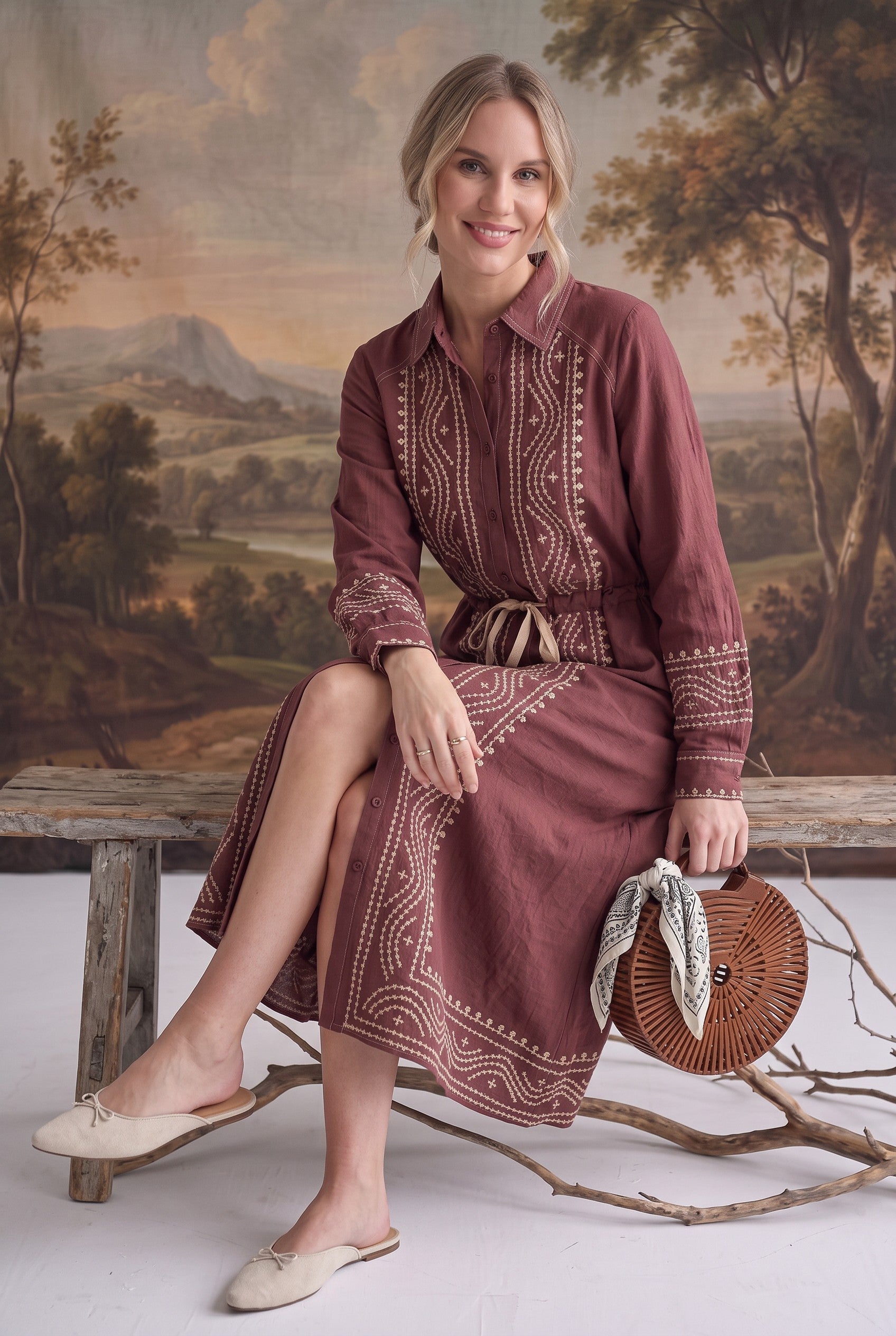 graced midi dress in maroon with contrast embroidery, button front, and drawstring waist worn by a seated woman