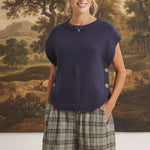 Model wearing a navy graced crew neck sweater vest with side button details, paired with plaid trousers.